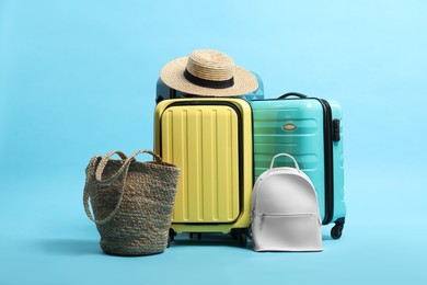 Photo of Colorful suitcases, backpack, beach bag and straw hat on light blue background