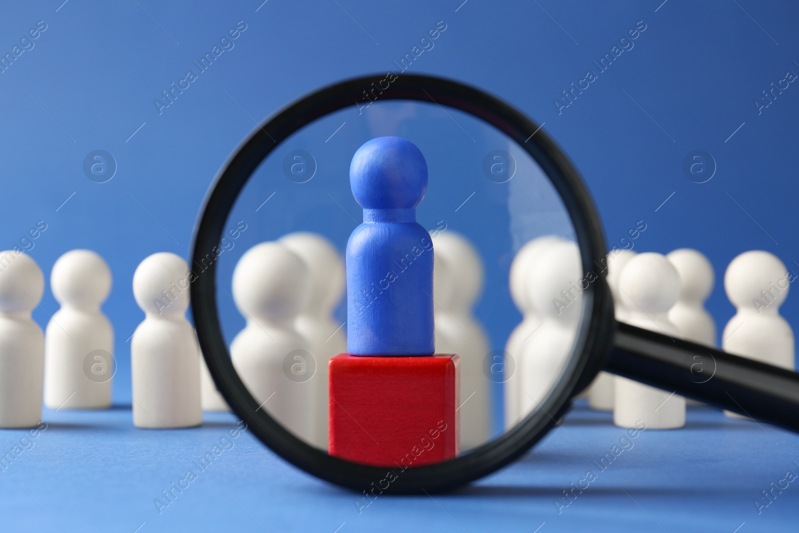 Photo of Competition concept. Looking through magnifying glass at human figure on wooden cube and other ones behind against blue background