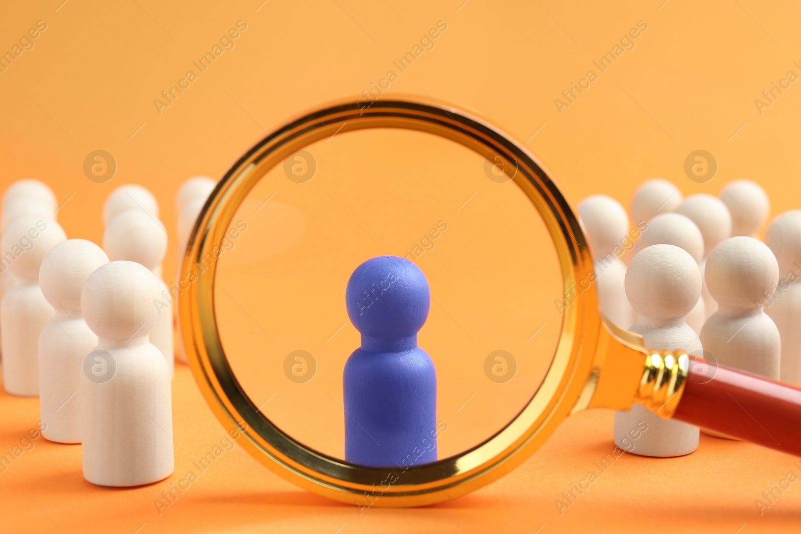 Photo of Looking at blue human figure through magnifying glass among other ones against orange background, closeup. Competition concept