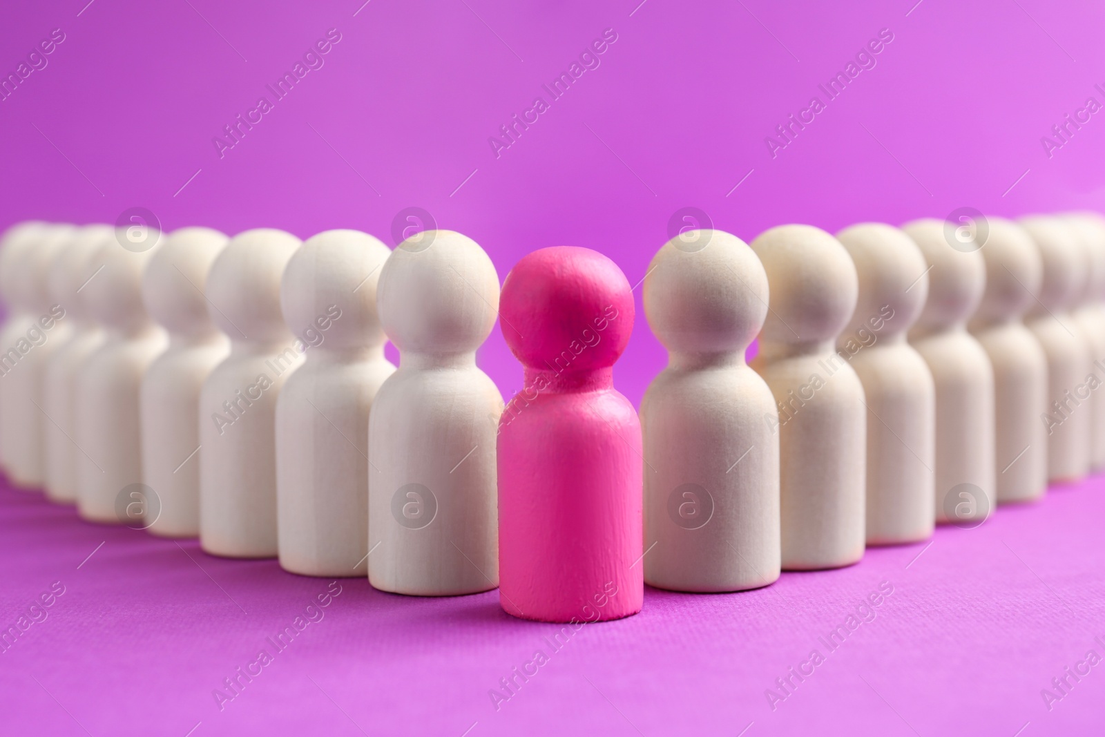 Photo of Pink human figure among wooden ones against violet background, closeup. Competition concept