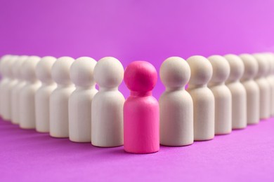 Photo of Pink human figure among wooden ones against violet background, closeup. Competition concept