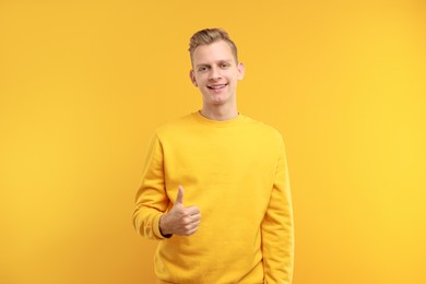 Photo of Happy man showing thumbs up on yellow background. Like gesture