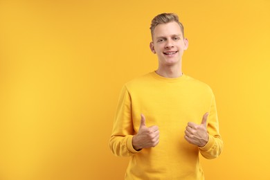 Photo of Happy man showing thumbs up on yellow background, space for text. Like gesture