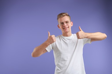 Photo of Happy man showing thumbs up on purple background, space for text. Like gesture