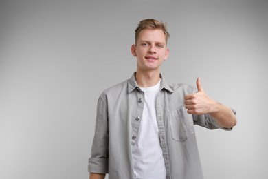 Photo of Happy man showing thumbs up on grey background, space for text. Like gesture