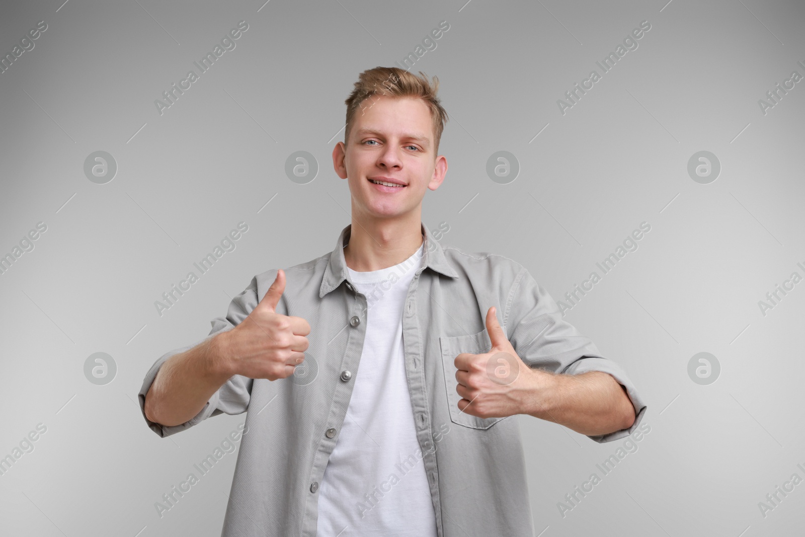 Photo of Happy man showing thumbs up on grey background. Like gesture