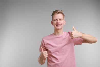 Photo of Happy man showing thumbs up on grey background, space for text. Like gesture