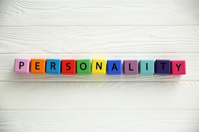 Photo of Word Personality made of colorful cubes with letters on white wooden table, top view