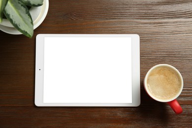 Photo of Tablet with blank screen, houseplant and coffee on wooden table, top view. Space for text