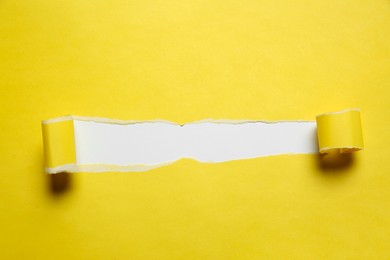 Photo of Yellow paper with torn hole on white background, top view. Space for text