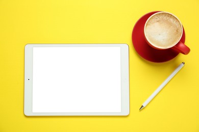 Photo of Tablet with blank screen and coffee on yellow background, top view. Space for design