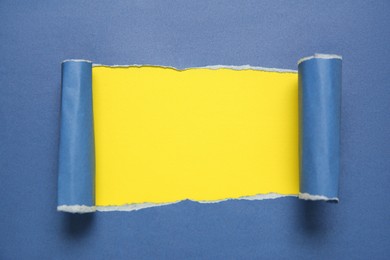 Photo of Blue paper with torn hole on yellow background, top view. Space for text