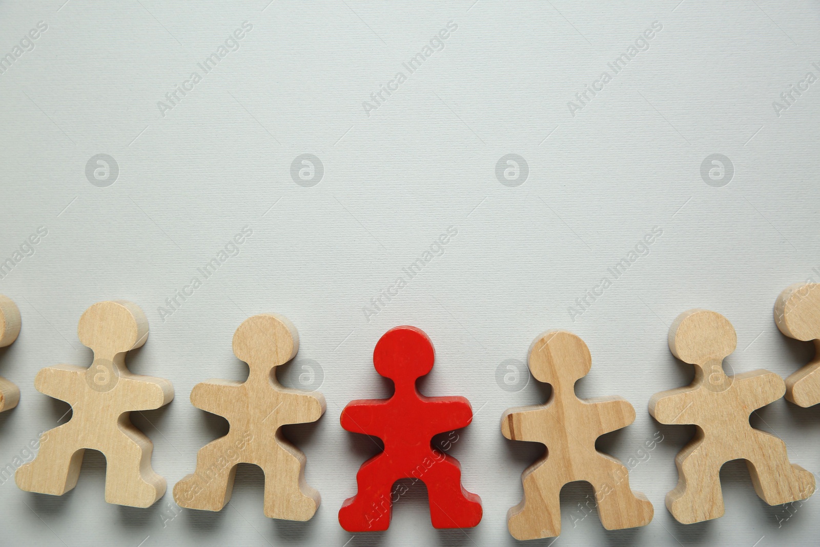 Photo of Personality concept. Red human figure among wooden ones on light grey background, flat lay. Space for text