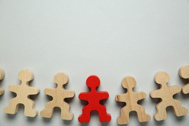 Photo of Personality concept. Red human figure among wooden ones on light grey background, flat lay. Space for text