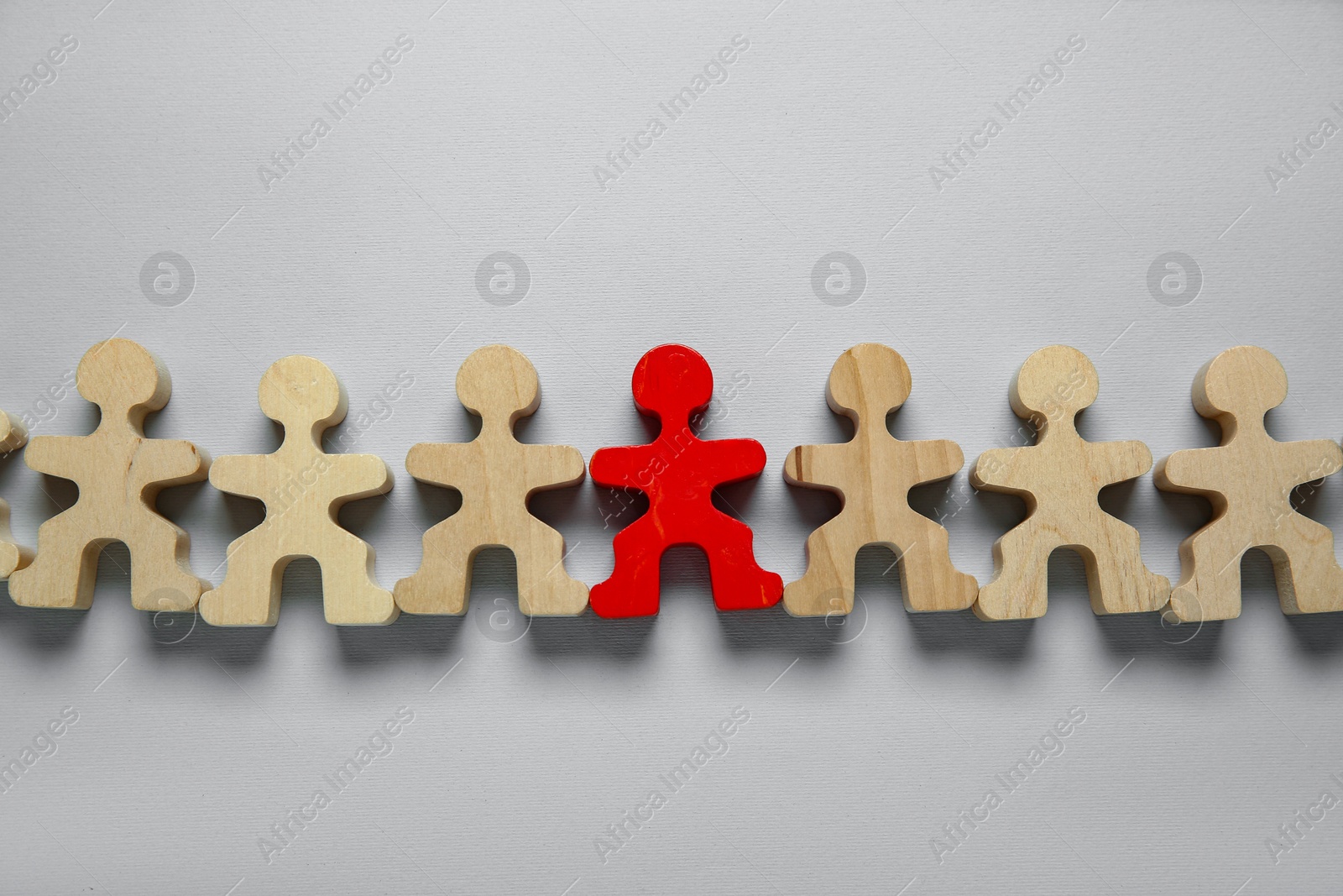 Photo of Personality concept. Red human figure among wooden ones on light grey background, flat lay