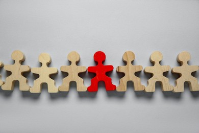 Photo of Personality concept. Red human figure among wooden ones on light grey background, flat lay