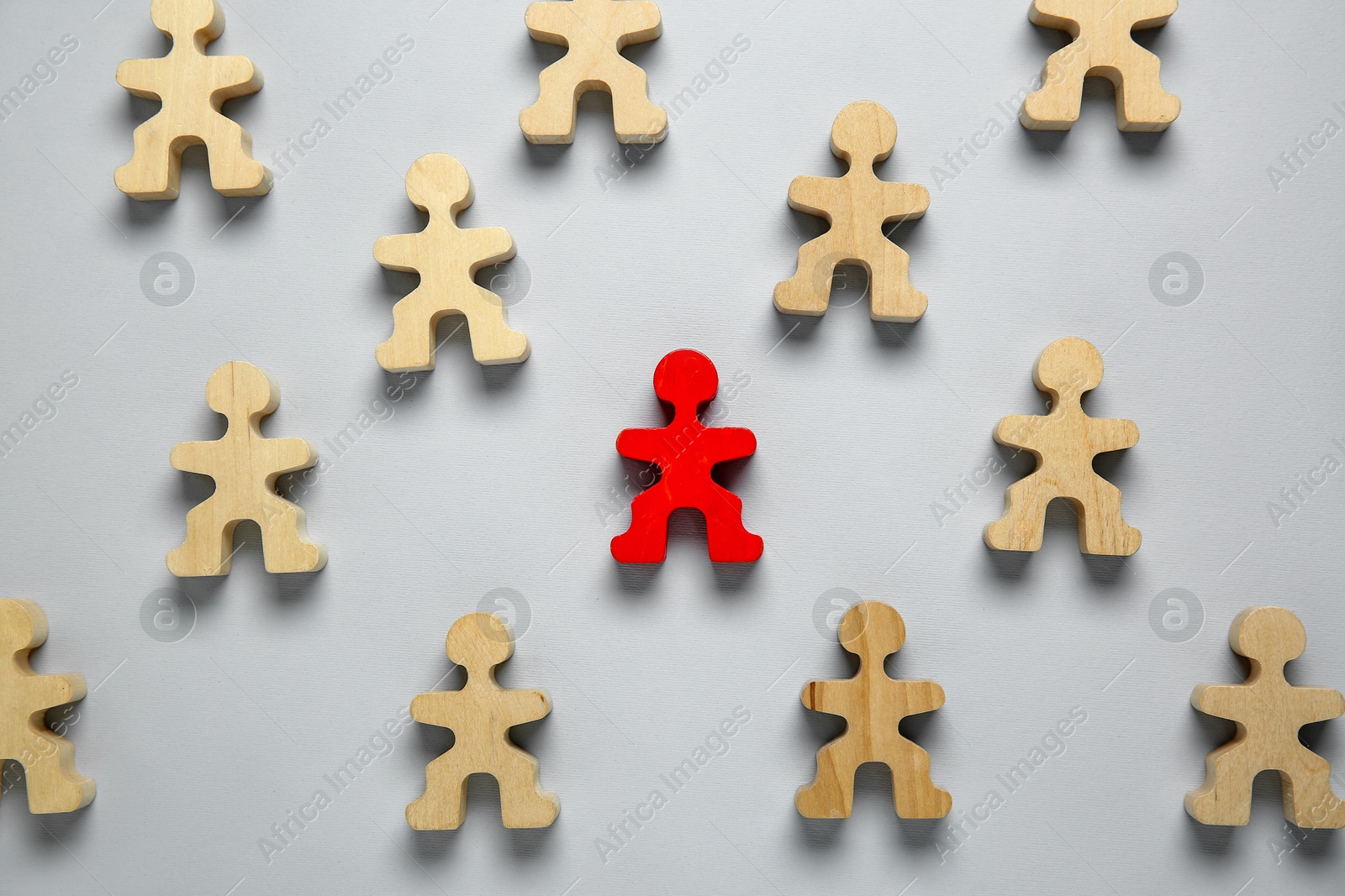 Photo of Personality concept. Red human figure among wooden ones on light grey background, flat lay