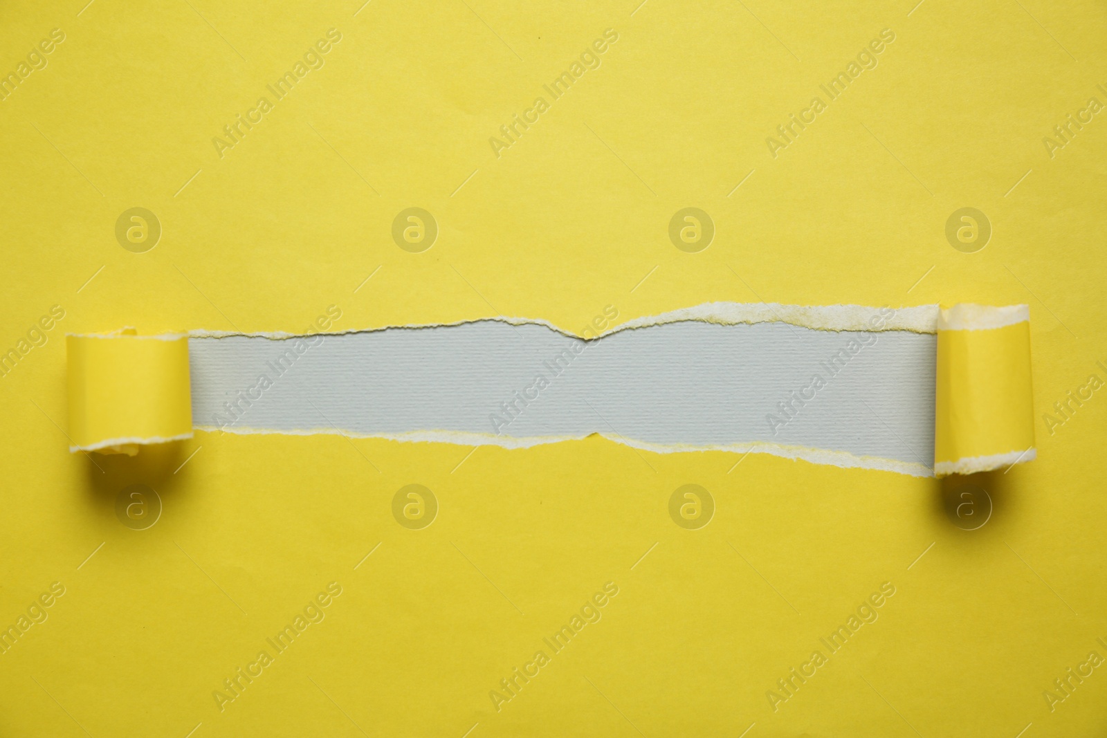 Photo of Yellow paper with torn hole on light grey background, top view. Space for text