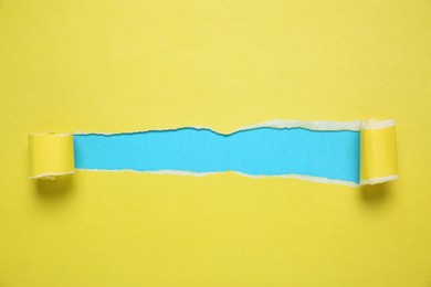 Photo of Yellow paper with torn hole on light blue background, top view. Space for text