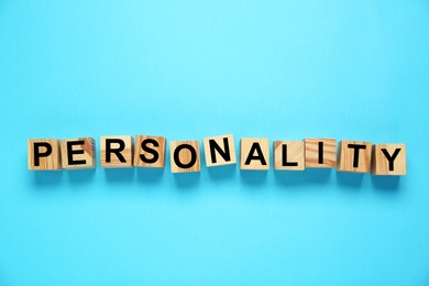 Photo of Word Personality made of wooden cubes with letters on light blue background, top view