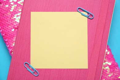 Photo of Blank note with paper clips and notebooks on light blue background, top view. Space for text