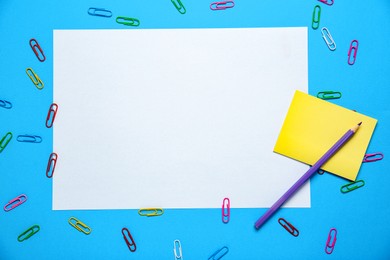 Photo of Blank sheet, pencil and paper clips on light blue background, flat lay. Space for text