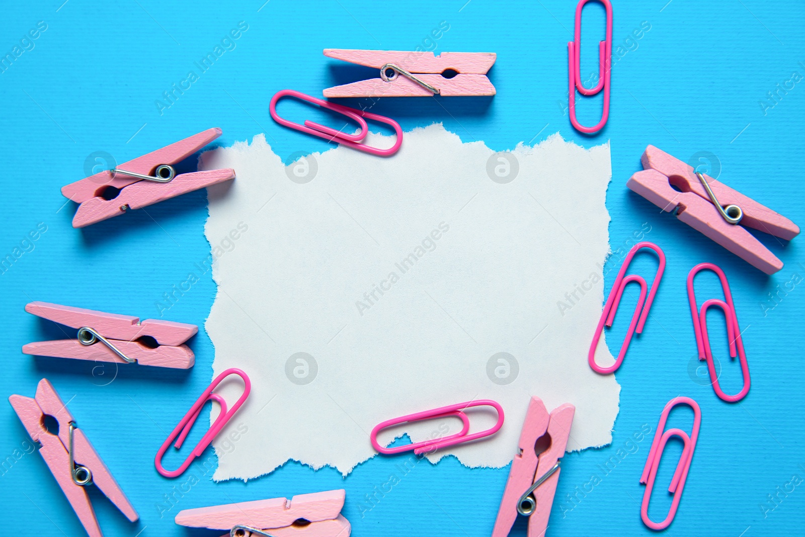 Photo of Blank note, clothing pegs and paper clips on light blue background, flat lay. Space for text