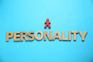 Photo of Word Personality made of wooden letters and red human figure on light blue background, top view