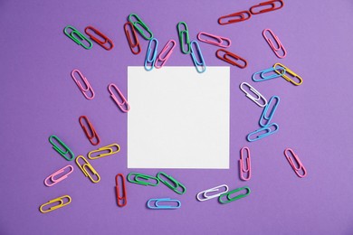 Photo of Blank note and paper clips on purple background, flat lay. Space for text