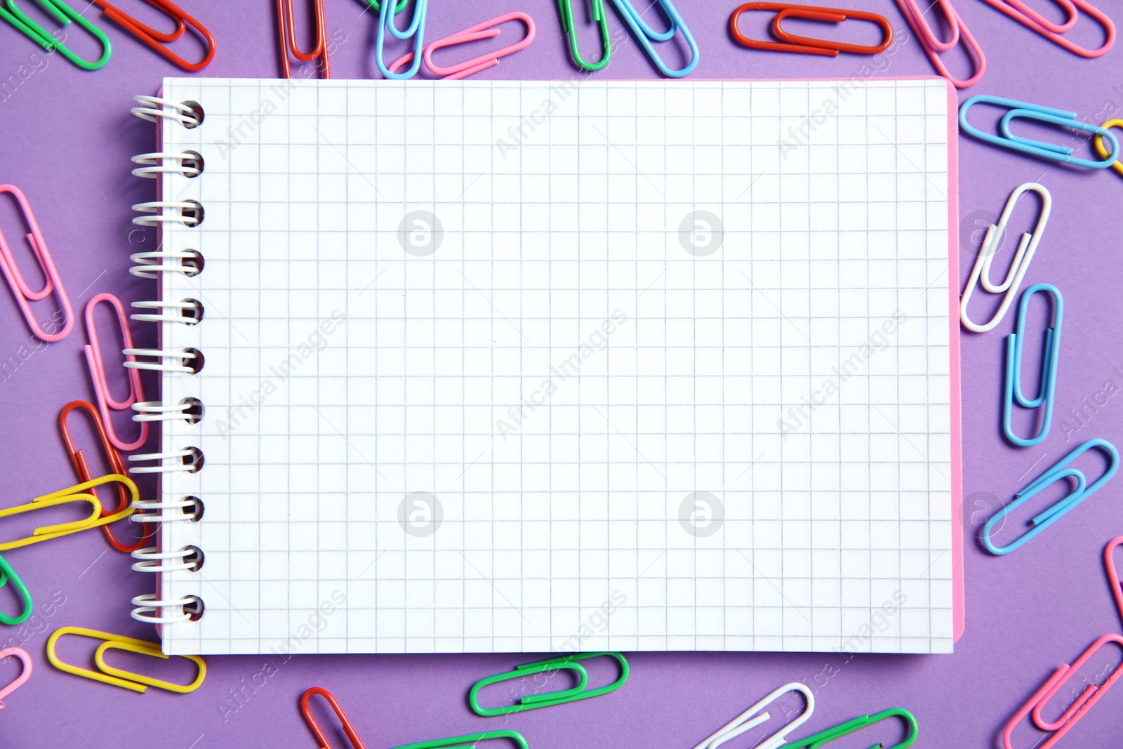 Photo of Blank notebook and paper clips on purple background, flat lay. Space for text