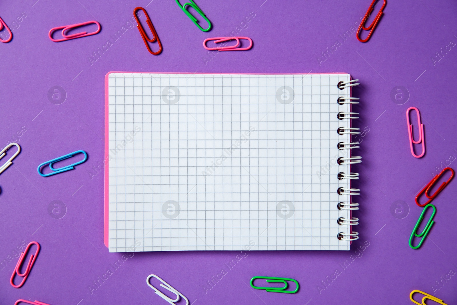 Photo of Blank notebook and paper clips on purple background, flat lay. Space for text