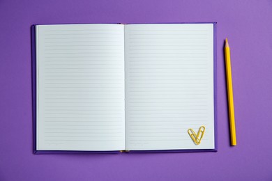 Photo of Blank notebook, paper clips and pencil on purple background, top view. Space for text