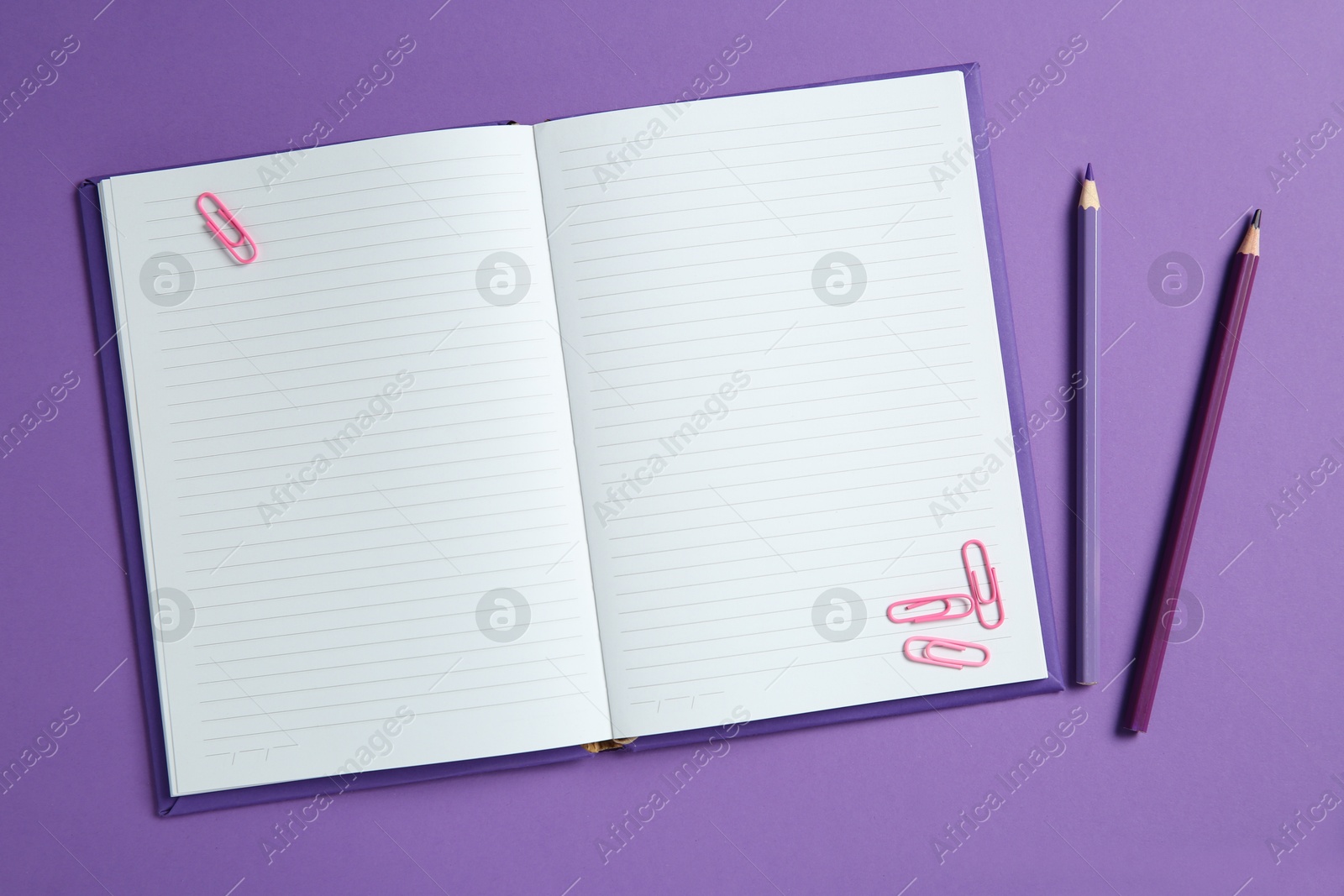 Photo of Blank notebook with paper clips and pencils on purple background, top view. Space for text