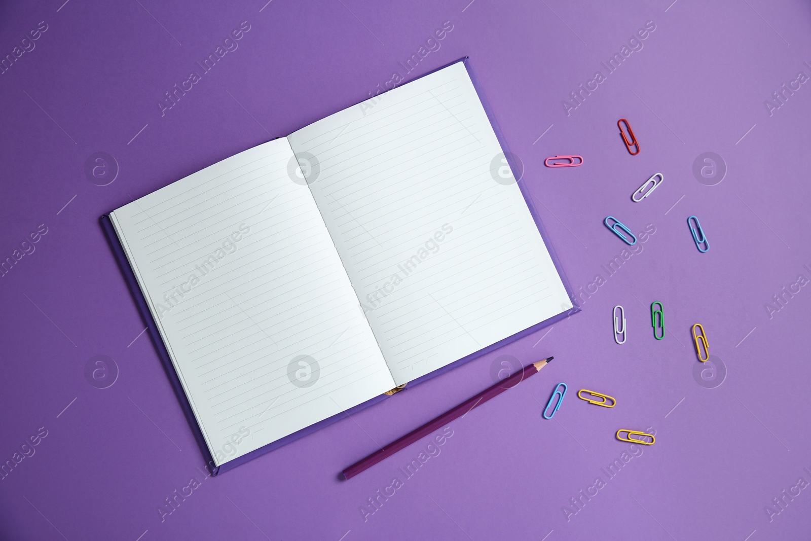 Photo of Blank notebook, paper clips and pencil on purple background, flat lay. Space for text