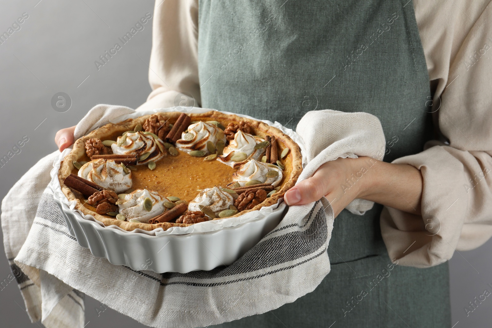 Photo of Woman holding homemade pumpkin pie with whipped cream, seeds and cinnamon on grey background, closeup