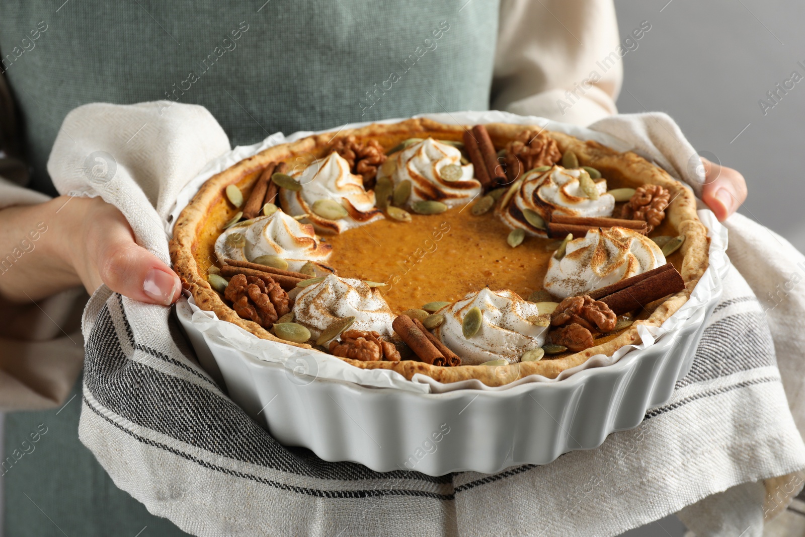 Photo of Woman holding homemade pumpkin pie with whipped cream, seeds and cinnamon on grey background, closeup