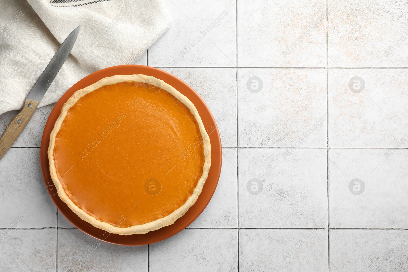 Photo of Tasty homemade pumpkin pie and knife on light tiled table, top view. Space for text