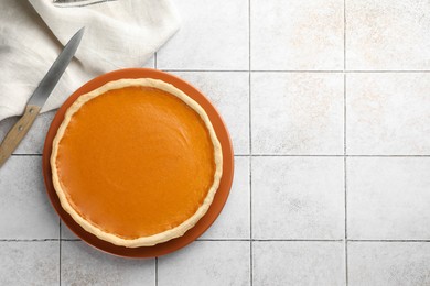 Photo of Tasty homemade pumpkin pie and knife on light tiled table, top view. Space for text