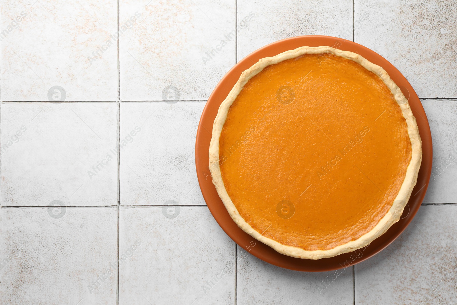 Photo of Tasty homemade pumpkin pie on light tiled table, top view. Space for text