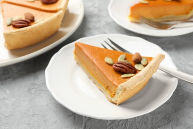 Photo of Pieces of tasty homemade pumpkin pie with seeds and nuts on grey table, closeup