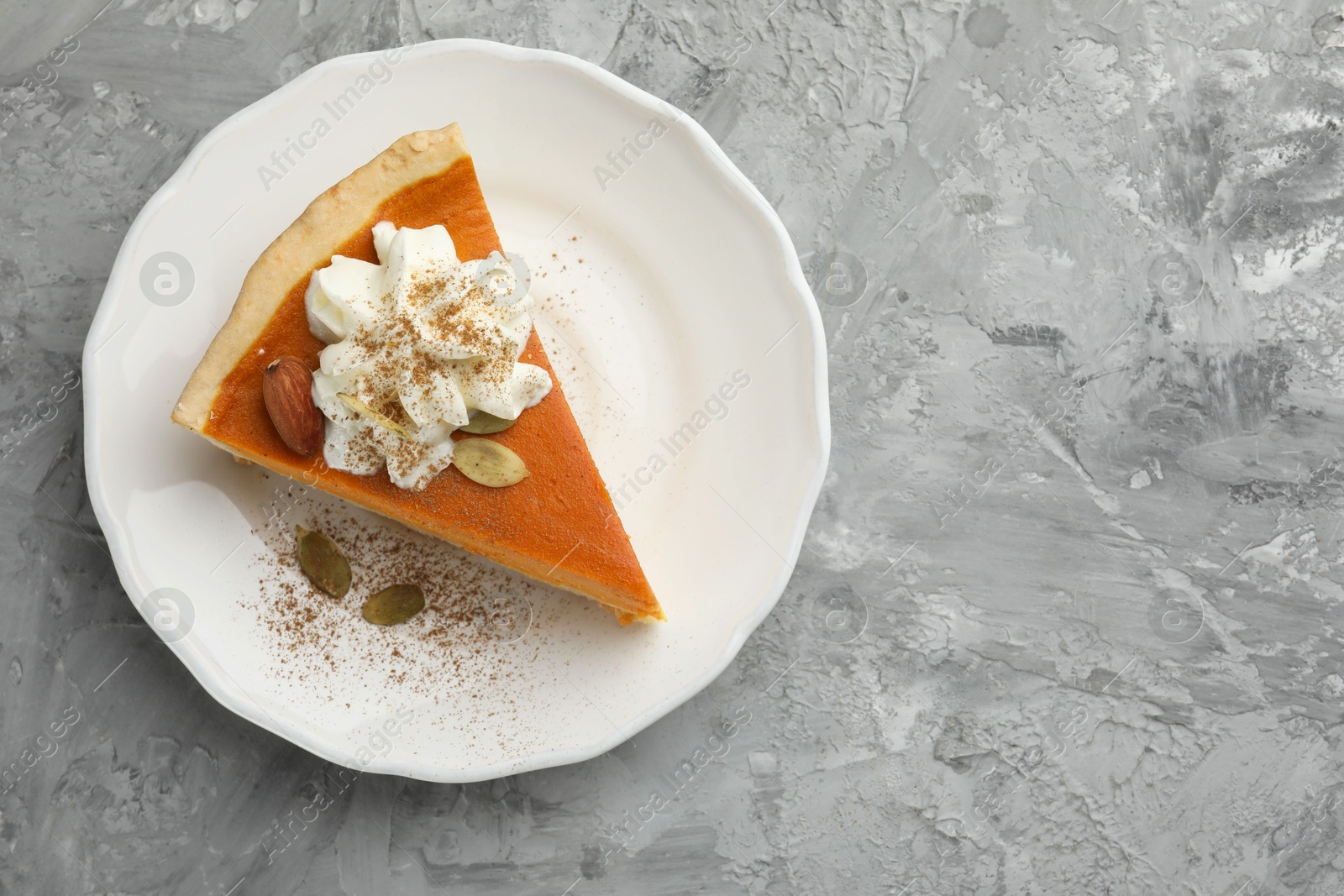 Photo of Piece of tasty homemade pumpkin pie with whipped cream, seeds and almond on grey table, top view. Space for text