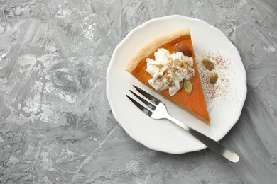 Photo of Piece of tasty homemade pumpkin pie with whipped cream, seeds and almond on grey table, top view. Space for text