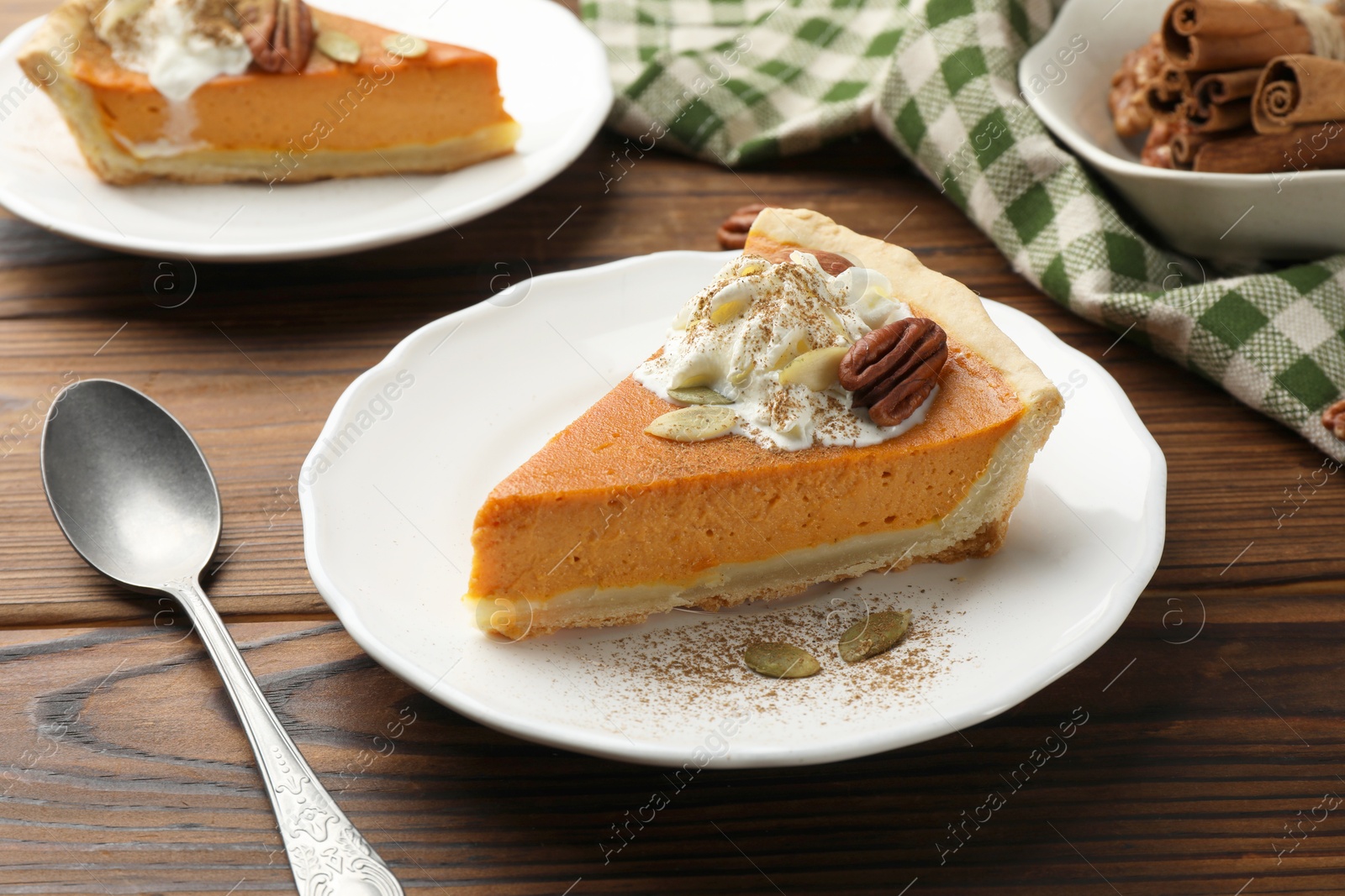 Photo of Piece of tasty homemade pumpkin pie with whipped cream, seeds and pecan nut on wooden table, closeup