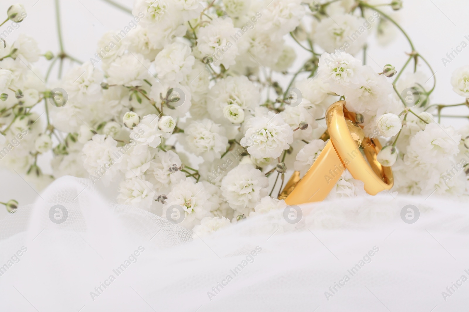 Photo of Golden wedding rings, veil and flowers on blurred background, closeup