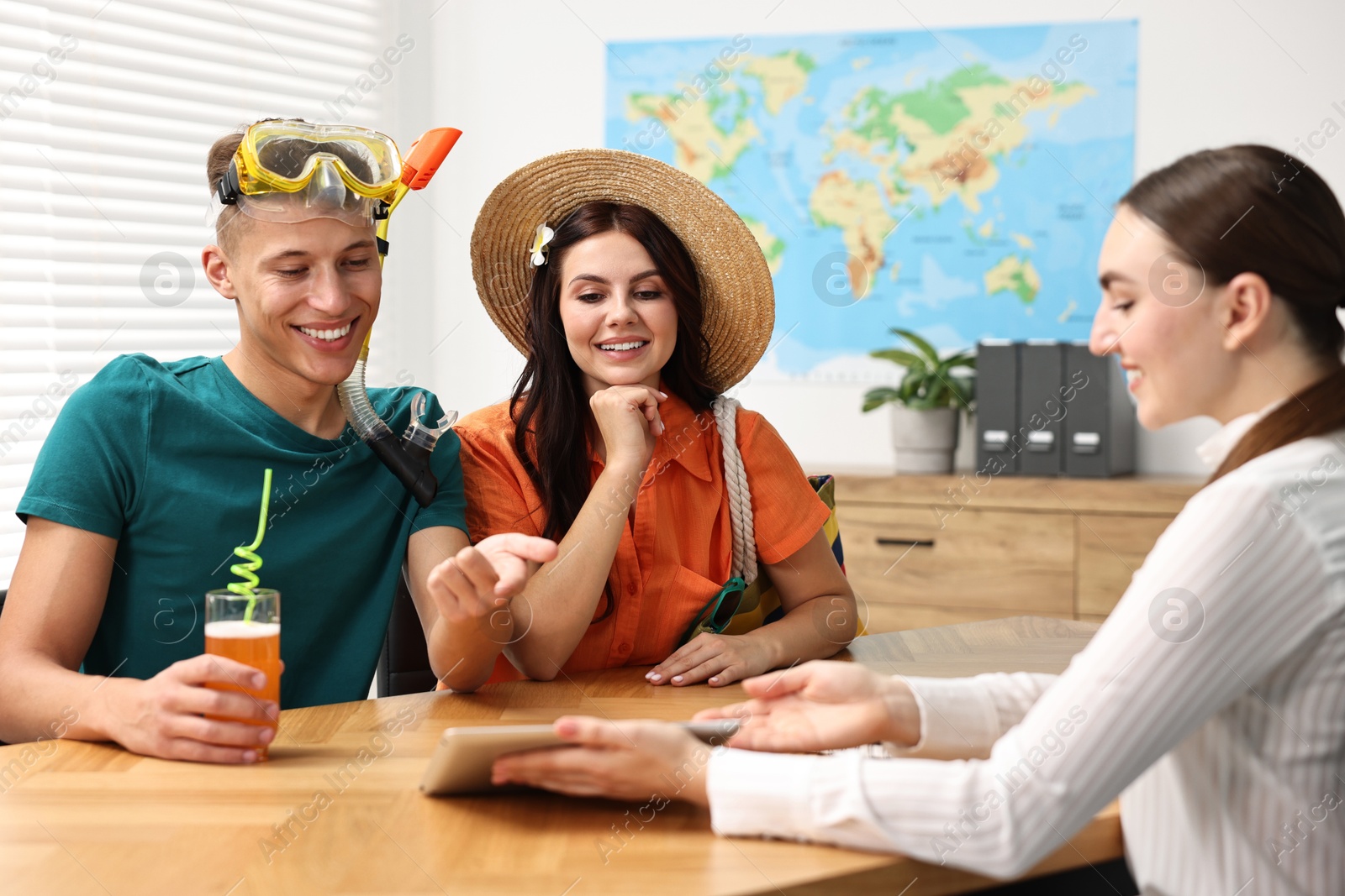 Photo of Happy couple planning vacation with travel agent at wooden table in office