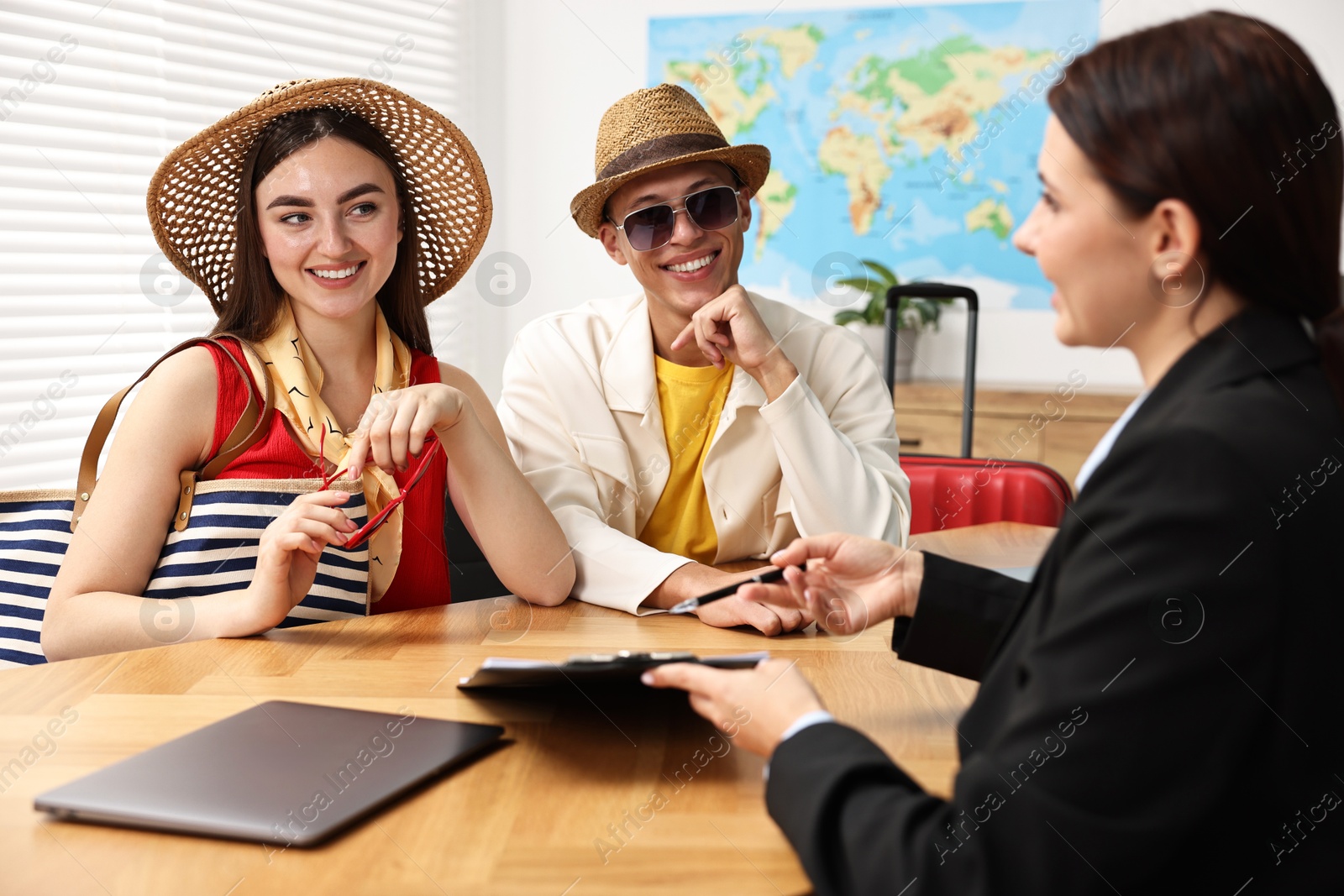 Photo of Happy couple planning vacation with travel agent at wooden table in office