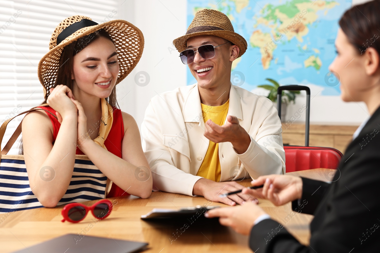 Photo of Happy couple planning vacation with travel agent at wooden table in office