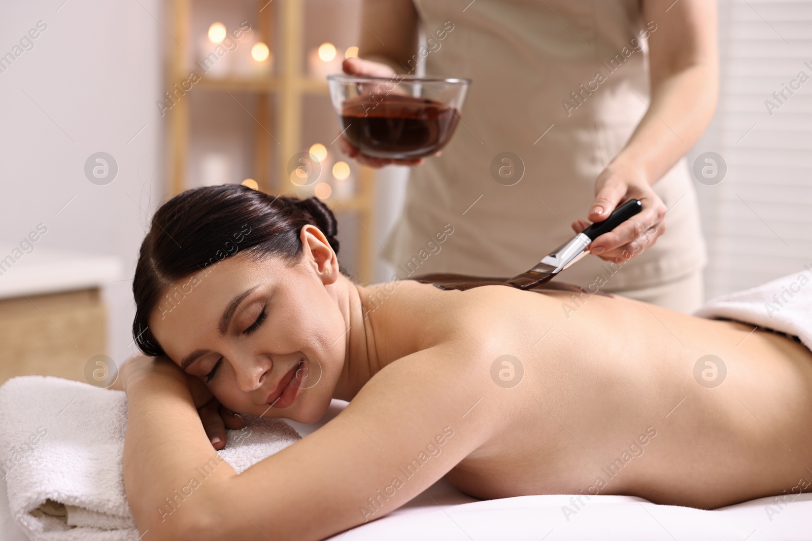 Photo of Chocolate body wrap. Spa worker applying mask onto woman's back in salon, closeup