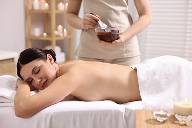 Spa worker with cosmetic product for chocolate body wrap near woman in salon, closeup