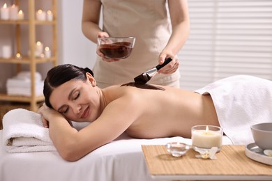 Photo of Chocolate body wrap. Spa worker applying mask onto woman's back in salon, closeup